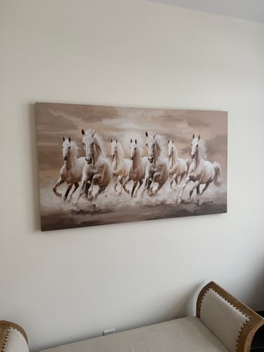 Customer's 'Seven White Running Horses' canvas print hung on a light wall above a sofa.