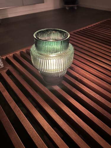 Recensent toont een close-up van de brandende groene, geribbelde POLSPOTTEN Steps waxinelichthouder op een houten oppervlak.