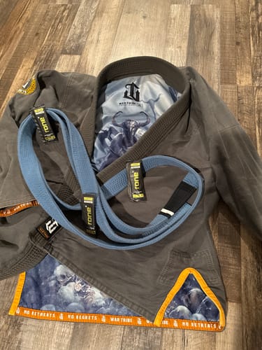 Customer's gray martial arts gi and blue belt laid out on a wooden floor, providing context for their review.