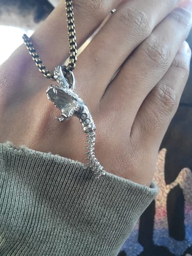 Close-up of a customer's hand holding the mystery item, a silver snake skeleton pendant on a chain.