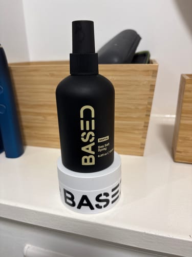 Customer's black bottle of Based Sea Salt Spray sitting on a white jar of the brand's hair clay.