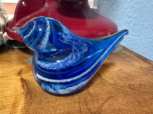 Customer's blue glass bird with white swirls of ash sitting on a wooden shelf.