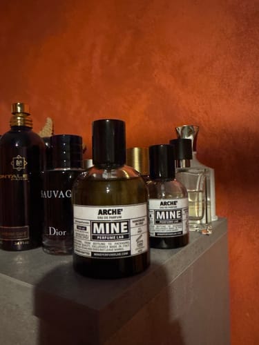 Cliente mostra i due flaconi di profumo ARCHÉ, quello nuovo da 100 ml e quello precedente da 50 ml, su una mensola.