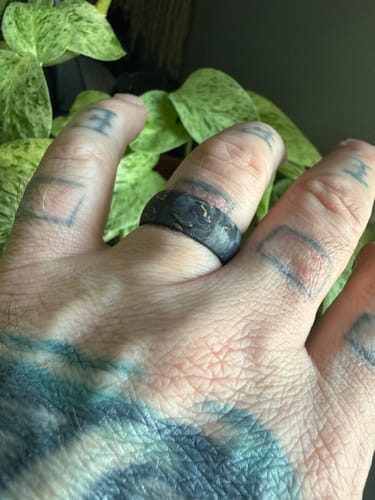 A customer's tattooed hand wearing The Grand Prix ring, showing its marbled black carbon fiber and gold design.