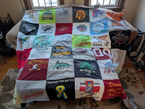 Customer's large Premium T-Shirt Quilt made from colorful hockey and sports jerseys, spread out on a sofa.