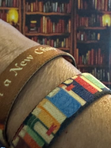 Close-up of a reviewer wearing the reversible Start a New Chapter Book Bracelet, showing both the text side and colorful book pattern.