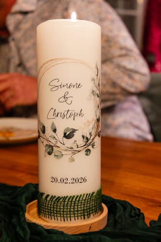 Die brennende Hochzeitskerze 'Floral Kreis' eines Kunden, personalisiert mit Namen und Datum auf einem Tisch.
