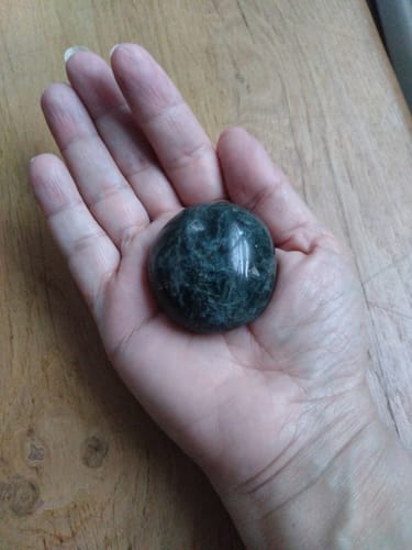 Avis d'un client montrant la pierre d'Apatite polie, de couleur foncée, dans la paume de sa main.