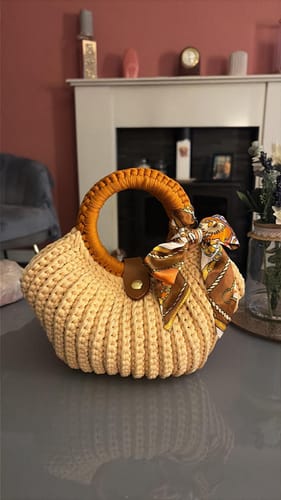 Customer's finished Shell crochet Handbag in light beige, featuring a round orange handle and a tied scarf.