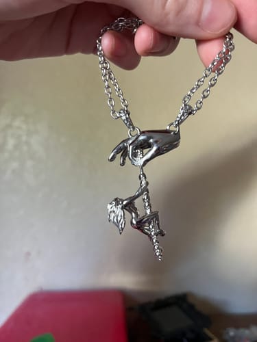 A customer's hand holding up the silver Dancing With Death Pendant, showing the detailed design of a figure on a pole.