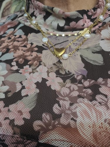 Close-up of a customer wearing the Riley Heart Necklace layered with other gold chains over a floral top.