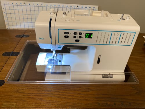 Customer's Sew Steady Custom Acrylic Cabinet Insert fitted perfectly around a white sewing machine in a wooden cabinet.