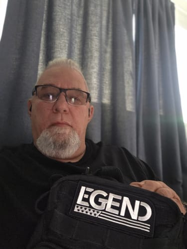 Customer with glasses and a gray goatee holding a black bag with a 'LEGEND' patch.
