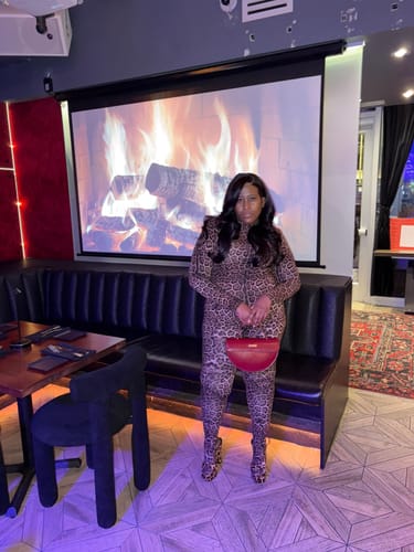 Reviewer shows a full-body view of the leopard-print Naked Print Closed Toe Jumpsuit in a lounge.