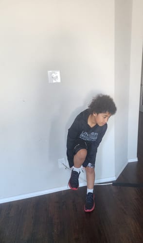 A young person wearing the black John 3:16 'The Cross' Youth Performance Shorts indoors.