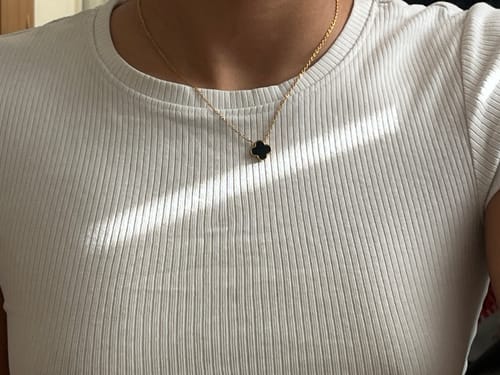 Kundin trägt die Black Clover Kette mit einem schwarzen Kleeblatt-Anhänger auf einem weißen Oberteil.