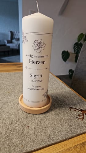 Rezensent zeigt die personalisierte Trauerkerze „Vintage Rosen“ auf einem Holzteller auf einem Tisch.