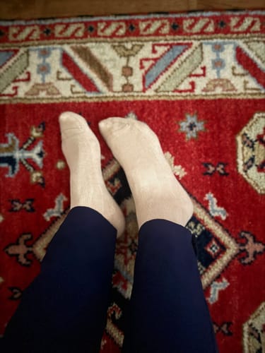 Customer wearing light-colored Performance Eucalyptus Compression Socks, resting their feet on a patterned rug.