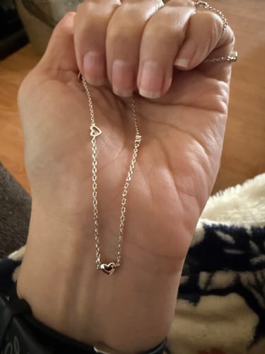 Customer holds up the Jane Heart Station Necklace, showing the delicate chain and small heart charms.