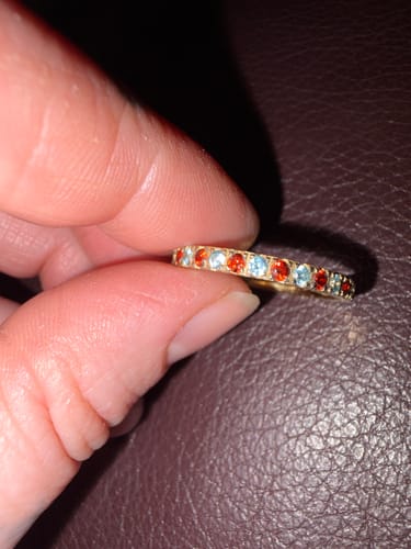 Close-up of a reviewer holding the Eterna Birthstone Ring with alternating sparkly red and blue stones.