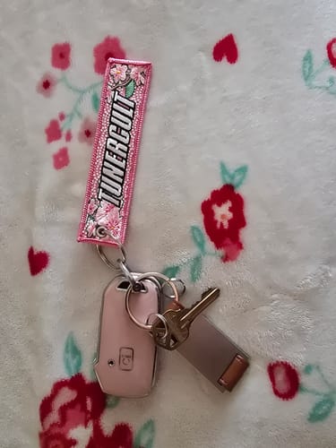 Customer's pink, embroidered SAKURA JET TAG attached to a set of keys with a pink fob on a floral blanket.
