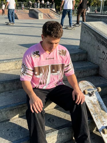 Reviewer wearing the Pink Flame Print Jersey T-shirt, sitting on steps at a skatepark with a skateboard.