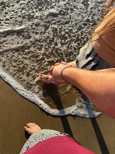 Cliente luciendo su Pulsera Cuban de 8mm en la playa, con los pies en el agua.