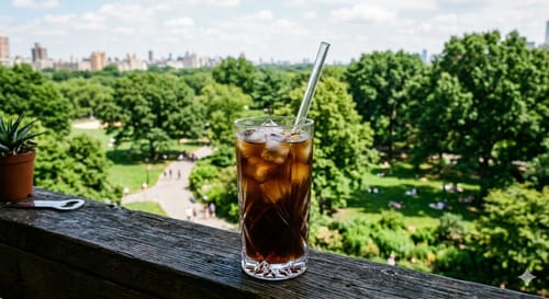 Reviewer's iced coffee from the Biweekly Surprise Plan, in a patterned glass on a railing overlooking a lush park.
