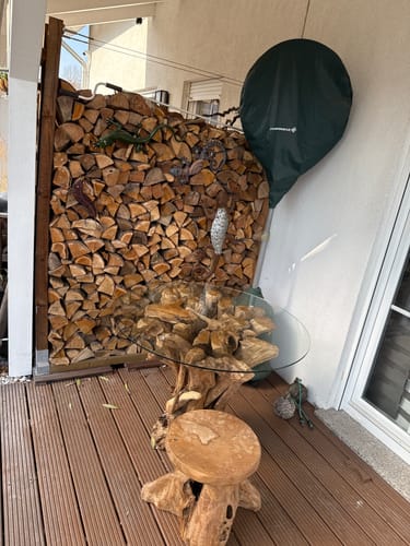 Kunde zeigt den Wurzelholz Esstisch IKAL mit seiner Glasplatte auf einer Holzterrasse.
