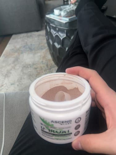 Customer holding an open white tub of D-BLOAT powder with a scoop resting inside.