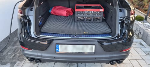 Klient pokazuje dopasowaną matę do bagażnika w otwartym bagażniku czarnego samochodu.