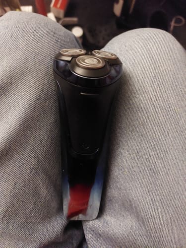 De klant toont het zwarte elektrische scheerapparaat met drie koppen, dat op zijn schoot rust.