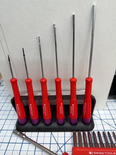 Customer's PB Swiss Tools screwdriver set with red handles neatly arranged in its black stand on a workbench.