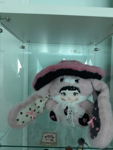 Reviewer's pink and black Caprielle Nommi Mushroom Hat plush displayed on a glass shelf.