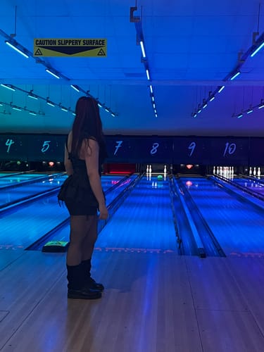 Reviewer wearing the Grunge Doll Stripes Flared Romper Dress from behind at a blue-lit bowling alley.
