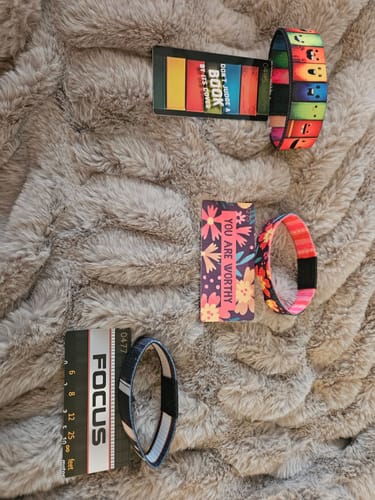 Reviewer displays three bracelets from a Mystery 3-Pack and their matching collector cards on a fluffy surface.