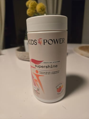 Photo d'un client montrant le flacon de vitamines SuperShine de Kids Power sur une table.