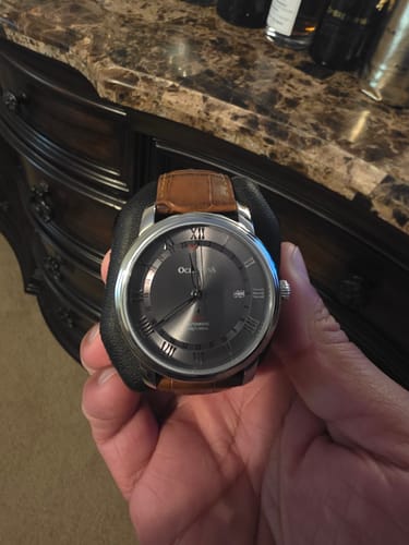 Customer holding the Oceaneva OceanTrek GMT watch with its gray dial and brown leather strap.