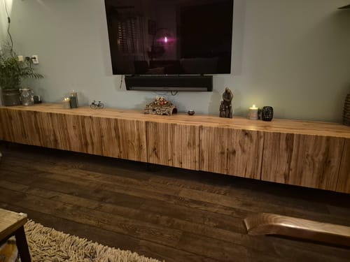 Klant toont het eiken TV-Meubel Vintar met lattenpatroon, opgesteld in de woonkamer.