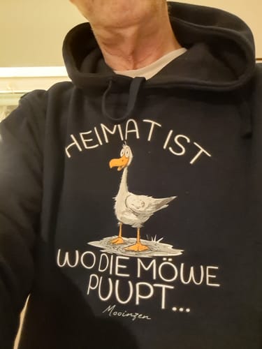Nahaufnahme eines Rezensenten, der den dunklen Möwe Nee Unisex Bio Hoodie mit dem Möwen-Aufdruck trägt.