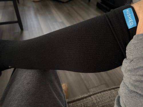 Reviewer wearing a black Hushed compression sock on their calf, showing the blue brand tag.