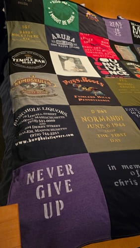 Customer's Premium T Shirt Quilt with varied colorful t-shirt squares laid across a bed.