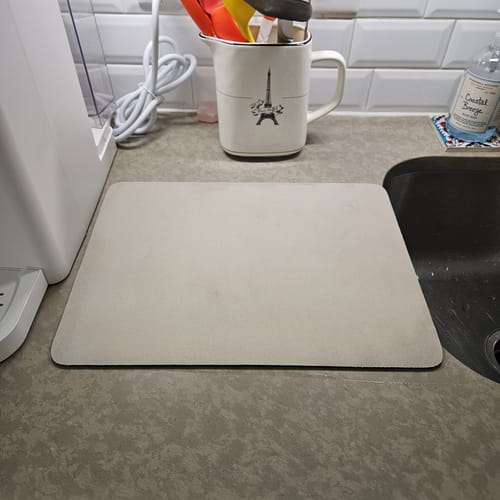Customer's light-colored Magic Dish Mat on a kitchen countertop next to the sink, showing its sleek profile.