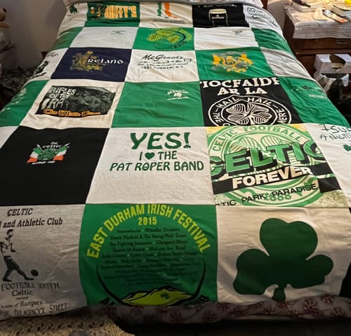 A reviewer's finished Premium T-Shirt Quilt with a green and white Irish theme, displayed across a bed.