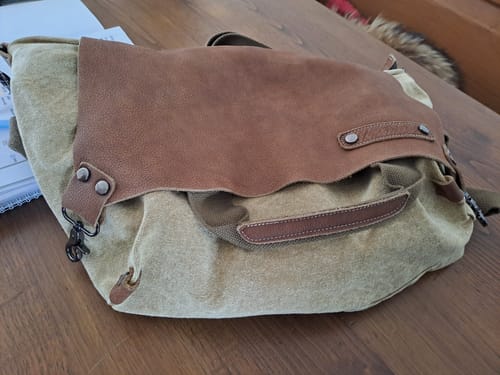 Customer's casual leather and canvas spliced shoulder bag resting on a wooden table.
