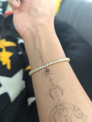 Close-up of a reviewer wearing the gold 3mm Tennis Chain Unisex Bracelet on their tattooed wrist.