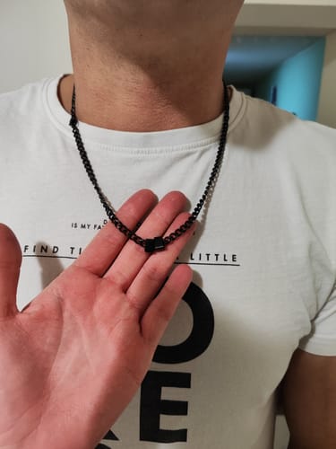 A customer wearing the black Legacy Necklace against a white t-shirt, holding the chain to show the bead detail.