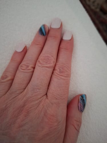 Hand einer Kundin, die die 'Spray Of Magic'-Folie als bunten Akzent auf Daumen und Zeigefinger zu weißen Nägeln trägt.