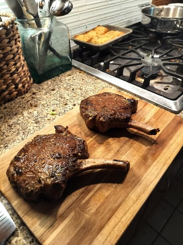 Reviewer's two cooked USDA Choice Bone-In Ribeye steaks resting on a wooden cutting board.