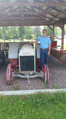 Customer, an older man, rests his hand on a vintage white and red tractor under a pavilion.